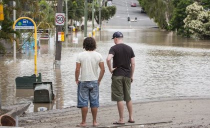Men looking at flood water across road. Adobe
